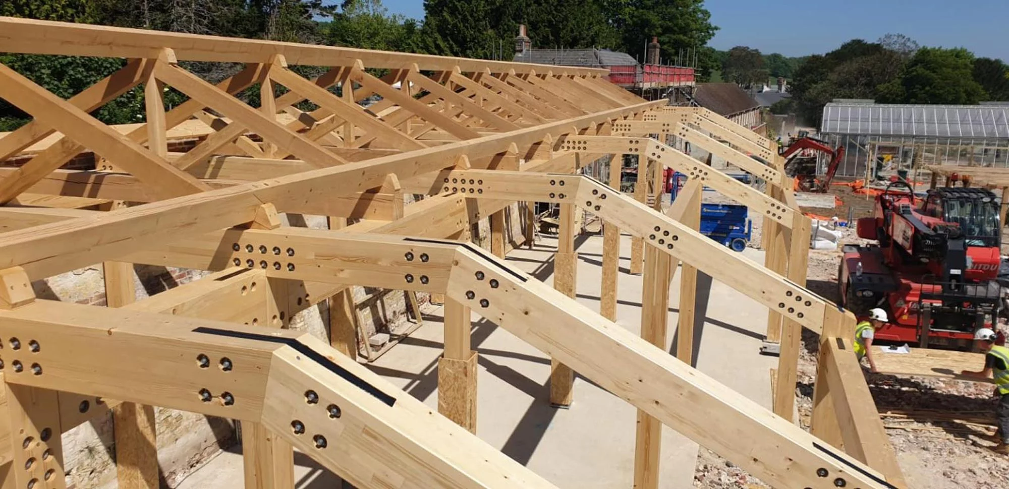 Wooden trusses being installed at a construction site showcase structural engineering in action, with workers, machinery, and other structures.