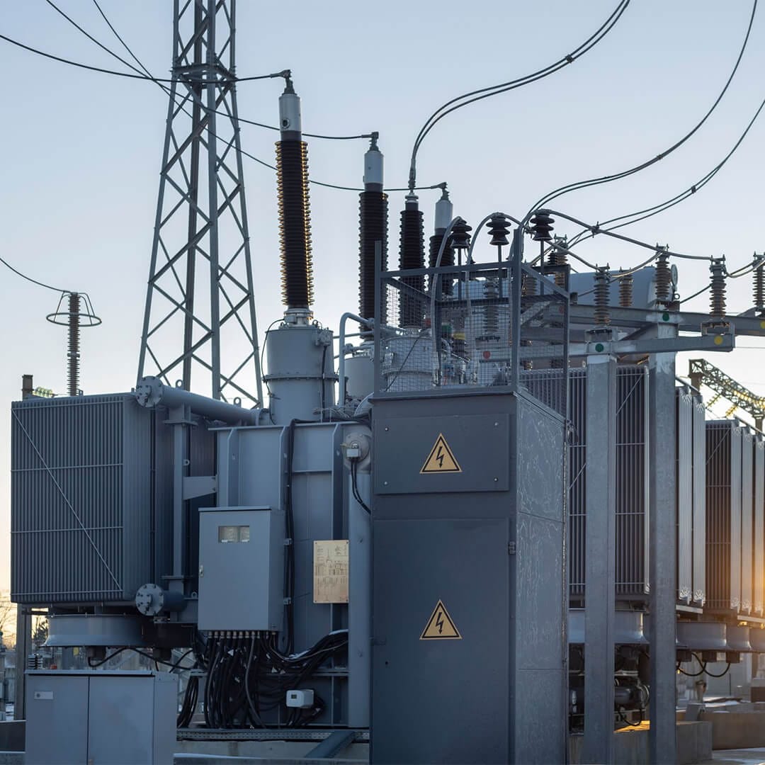 Outdoor electrical substation with transformers, power lines, and warning signs indicating high voltage.