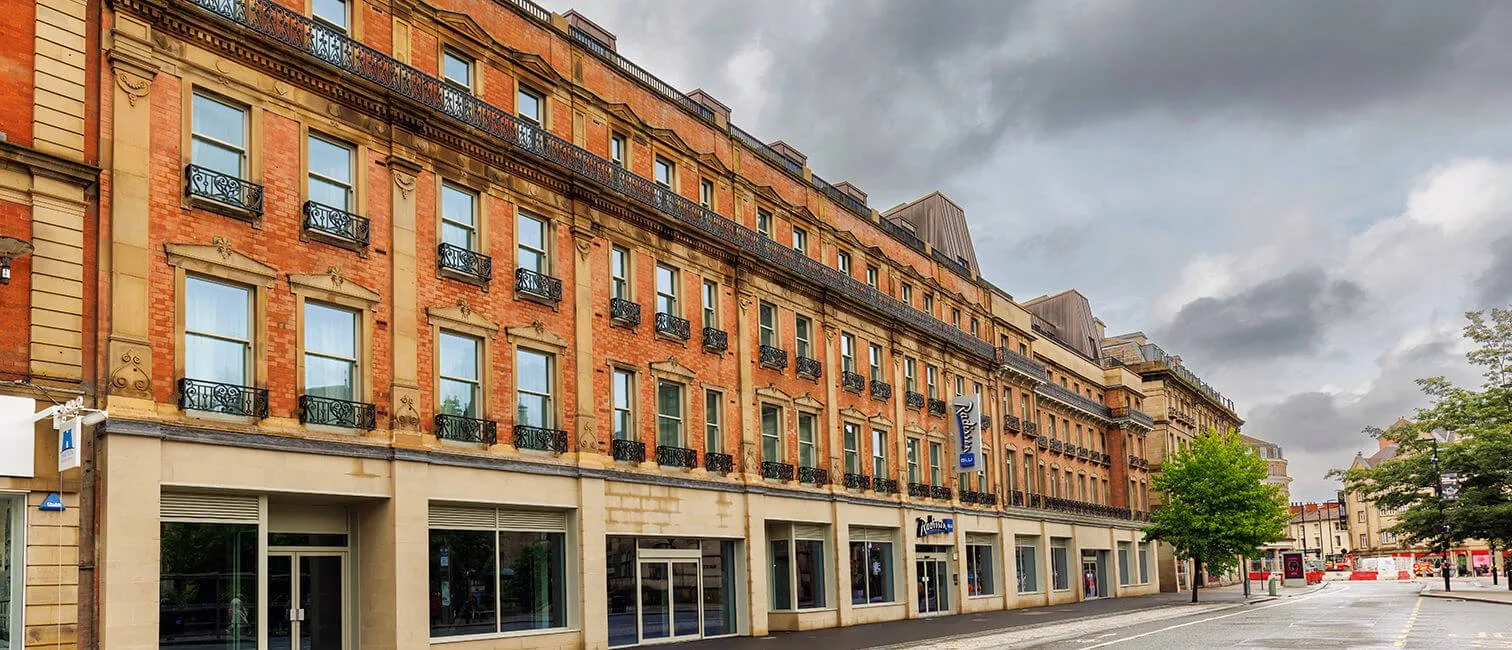 A multi-storey brick and stone building, designed with civil engineering precision, features large windows and black railings on a quiet, empty street beneath a cloudy sky.