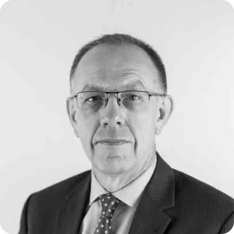 A middle-aged man wearing glasses, a suit, and a polka dot tie, poses for a formal portrait against a plain background.