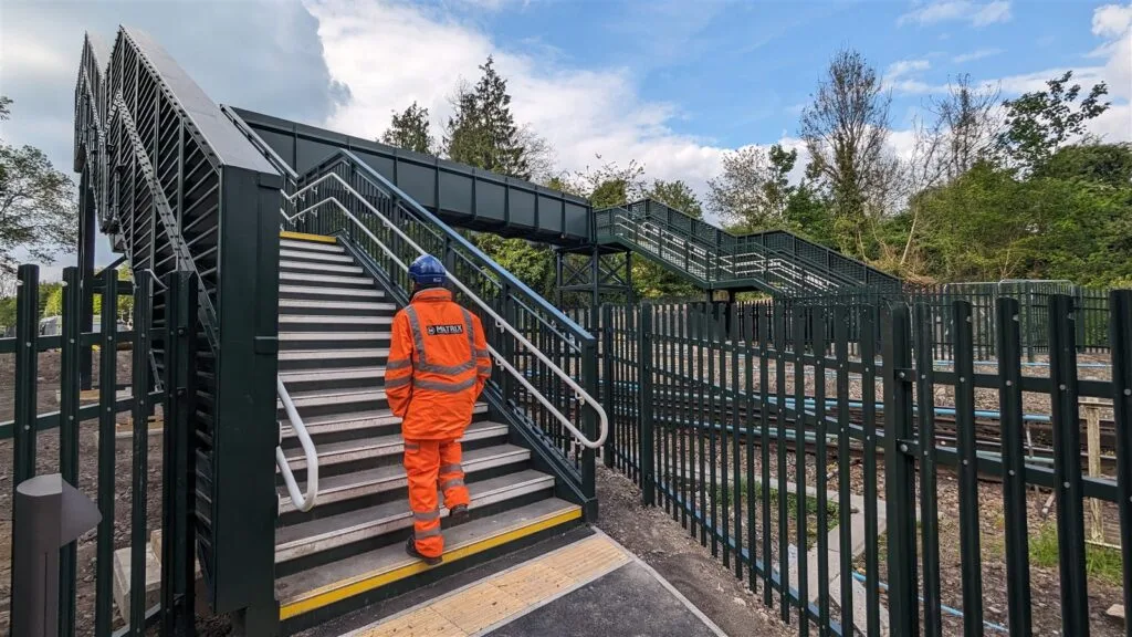 A Matrix Consulting Engineers engineer in orange PPE climbing the steps of a newly completed steel footbridge over electrified railway lines at Tottenham Hale Station.