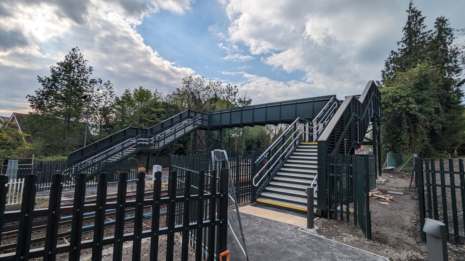 Side view of a completed steel footbridge over a railway, with a stair flight at each end of the span.