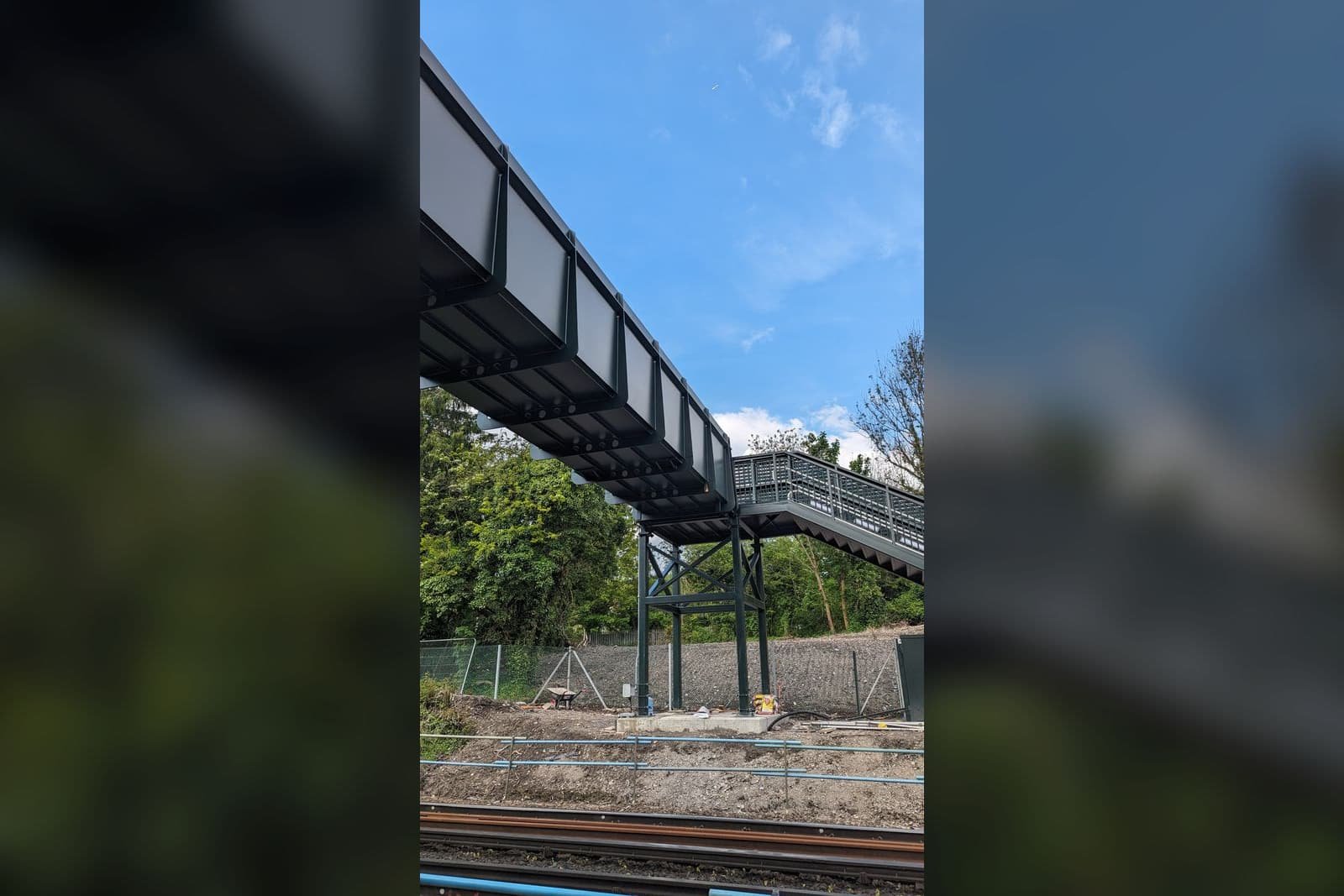 A completed footbridge span seen from below as it crosses above the running lines, showing the soffit clearance.