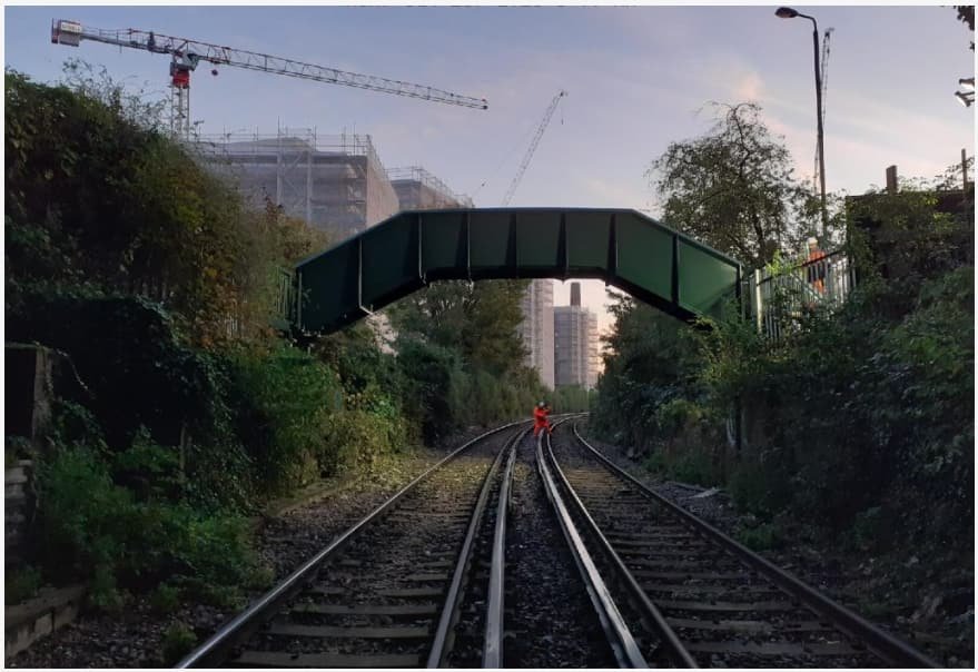 Footbridge crossing a railway in a deep urban cutting at Mount Street, with tower cranes and apartment blocks beyond.